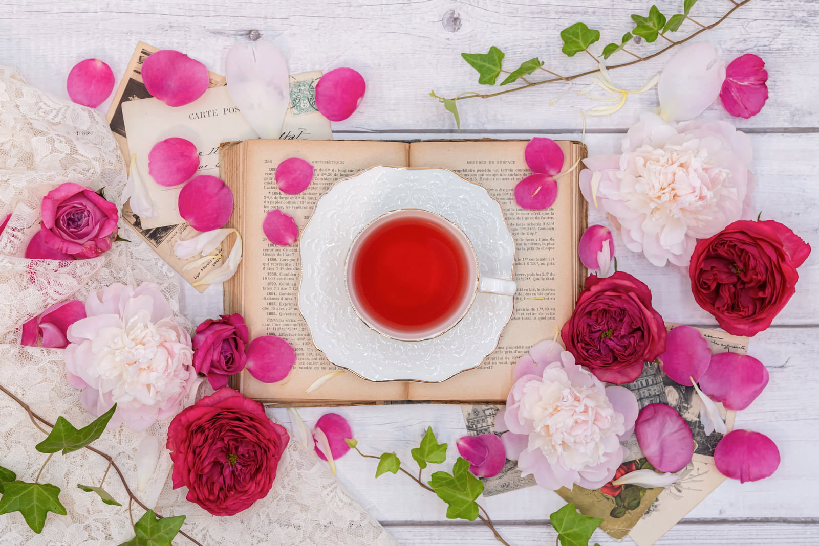 白いテーブルに置かれた紅茶のカップと散らばる赤い薔薇の花びら
