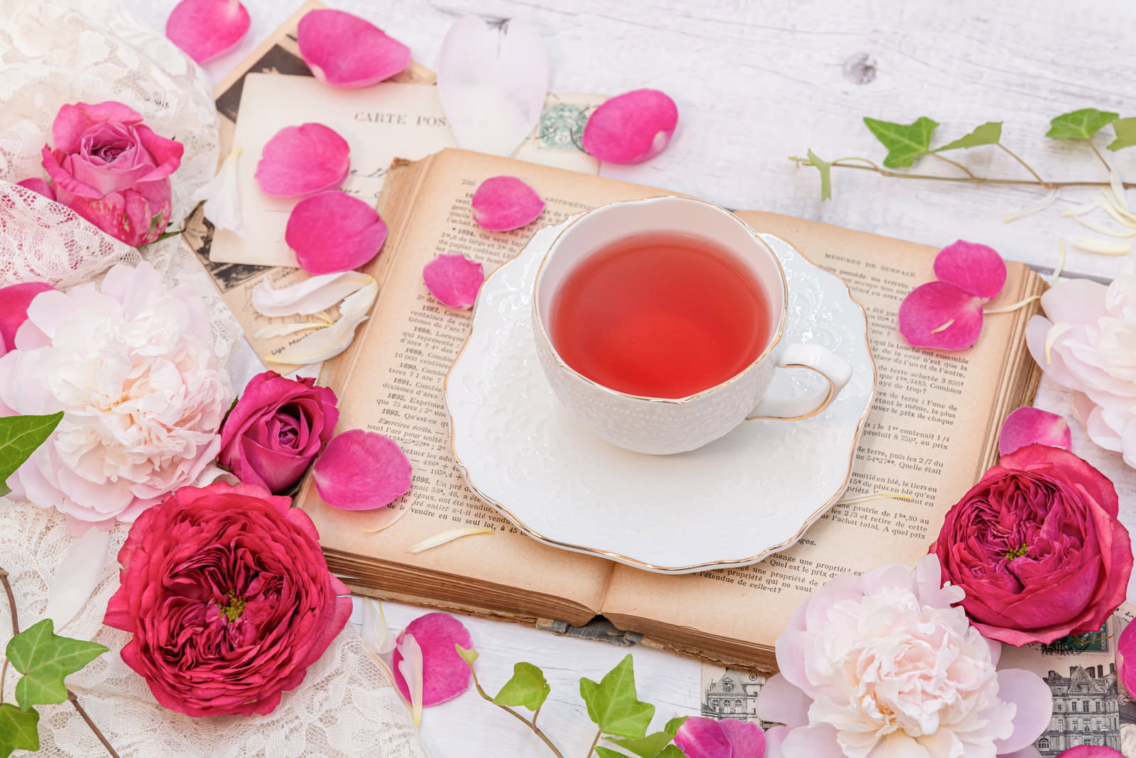 白いティーカップに入った赤い紅茶とピンクのバラの花びら、洋書が配置された上品なティータイムの様子