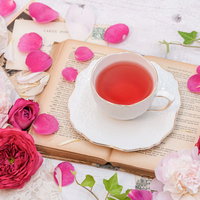 ピンクのバラの花びらに囲まれた洋書とローズティーの写真