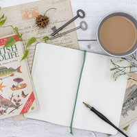 木製テーブルに置いた白紙のメモ帳と図鑑、ペンと小物の写真