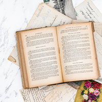 大理石調の表面に散らばる手紙や絵はがきの上に開かれた古書の写真