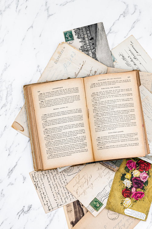 大理石調の表面に散らばる手紙や絵はがきの上に開かれた古書