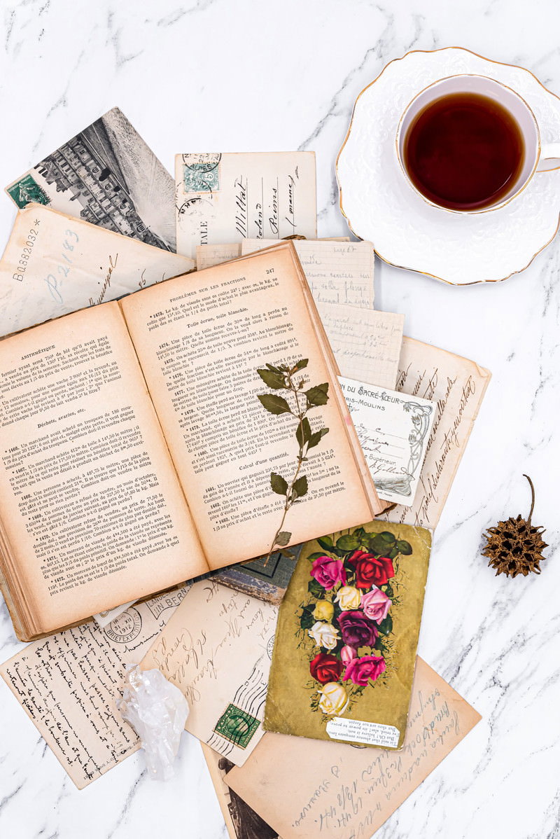 古書や手紙が散らばるテーブルの上に置かれたコーヒーカップと押し花