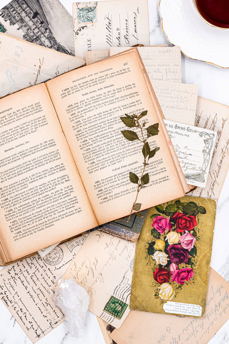 開かれた洋書に押し花が挟まれ、周りに手紙や絵はがきが散らばる様子