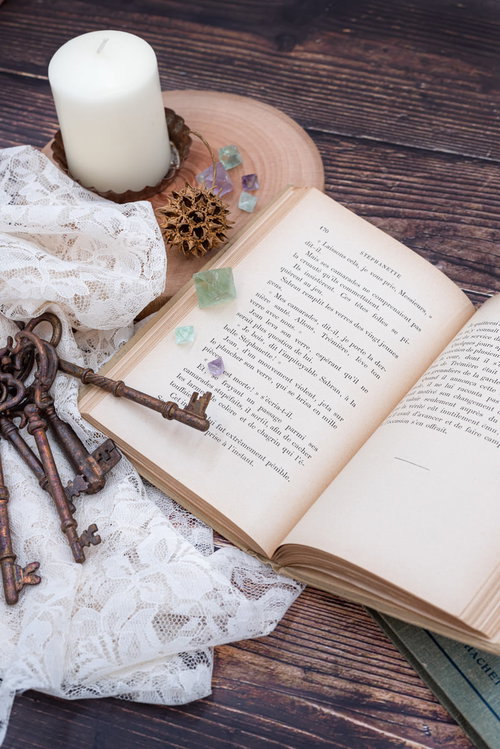 木製テーブルに開いた洋書と古書、鍵の束とキャンドル