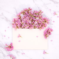 大理石の上に咲き溢れるピンク色の生花が詰まった封筒の写真