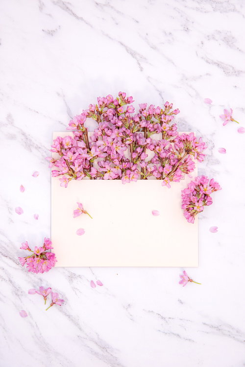 大理石の上に咲き溢れるピンク色の生花が詰まった封筒