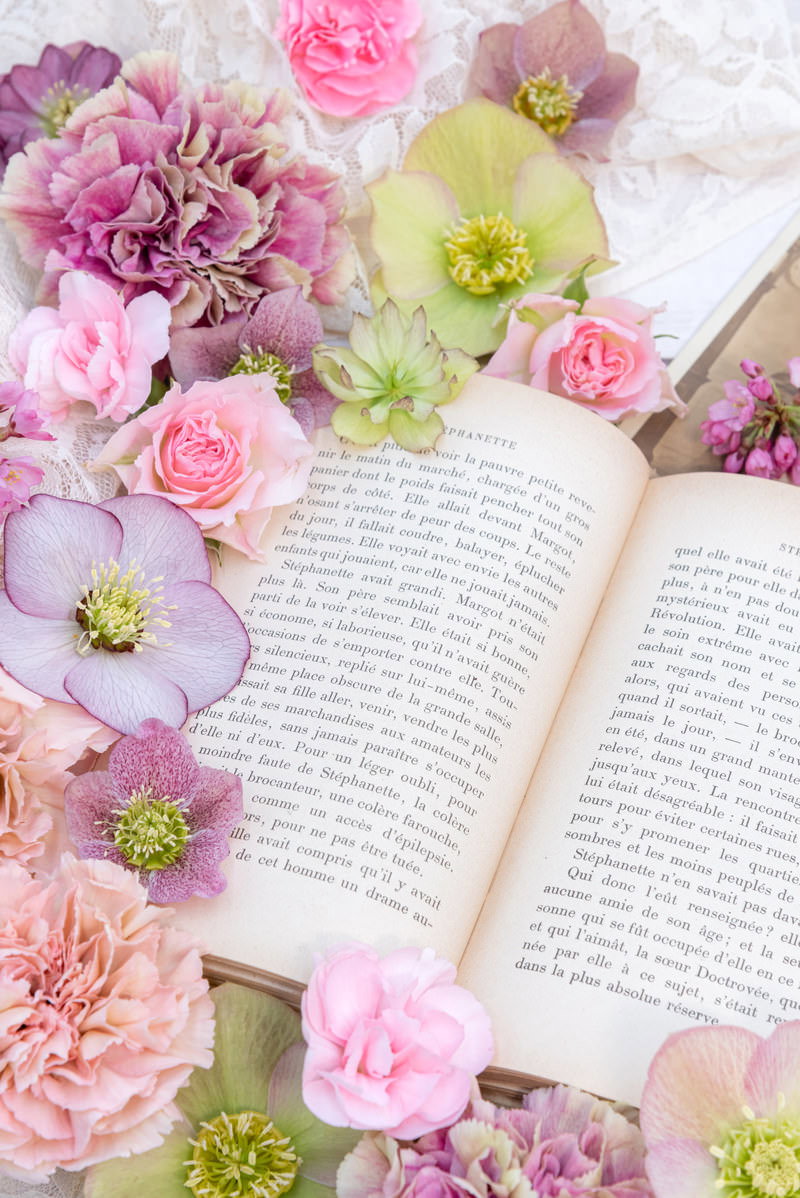 開かれた洋書の周りにピンクやパープルの花が配置された写真