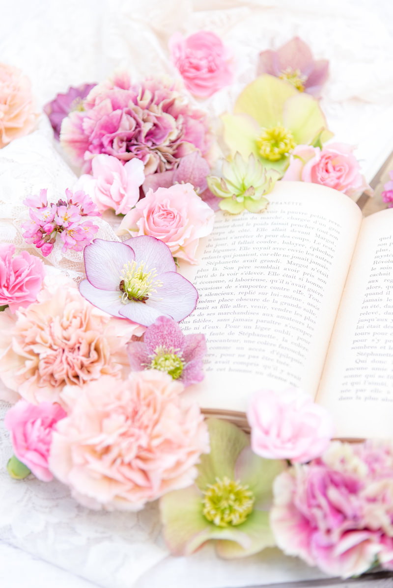 開いた洋書のページにピンクのカーネーションやガーベラが沿うように配置された写真
