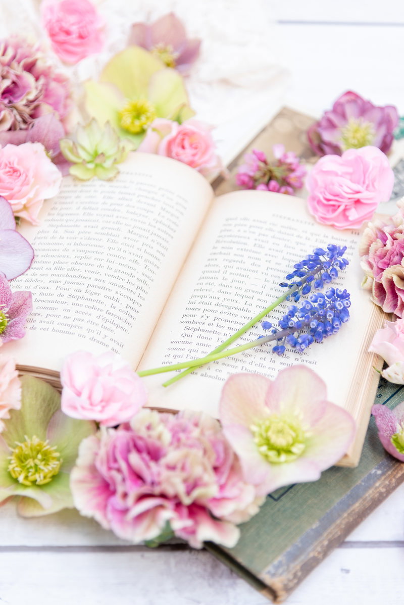 開かれた洋書の上にピンクや白のカーネーション、黄色のガーベラが配置された花と本のアレンジメント