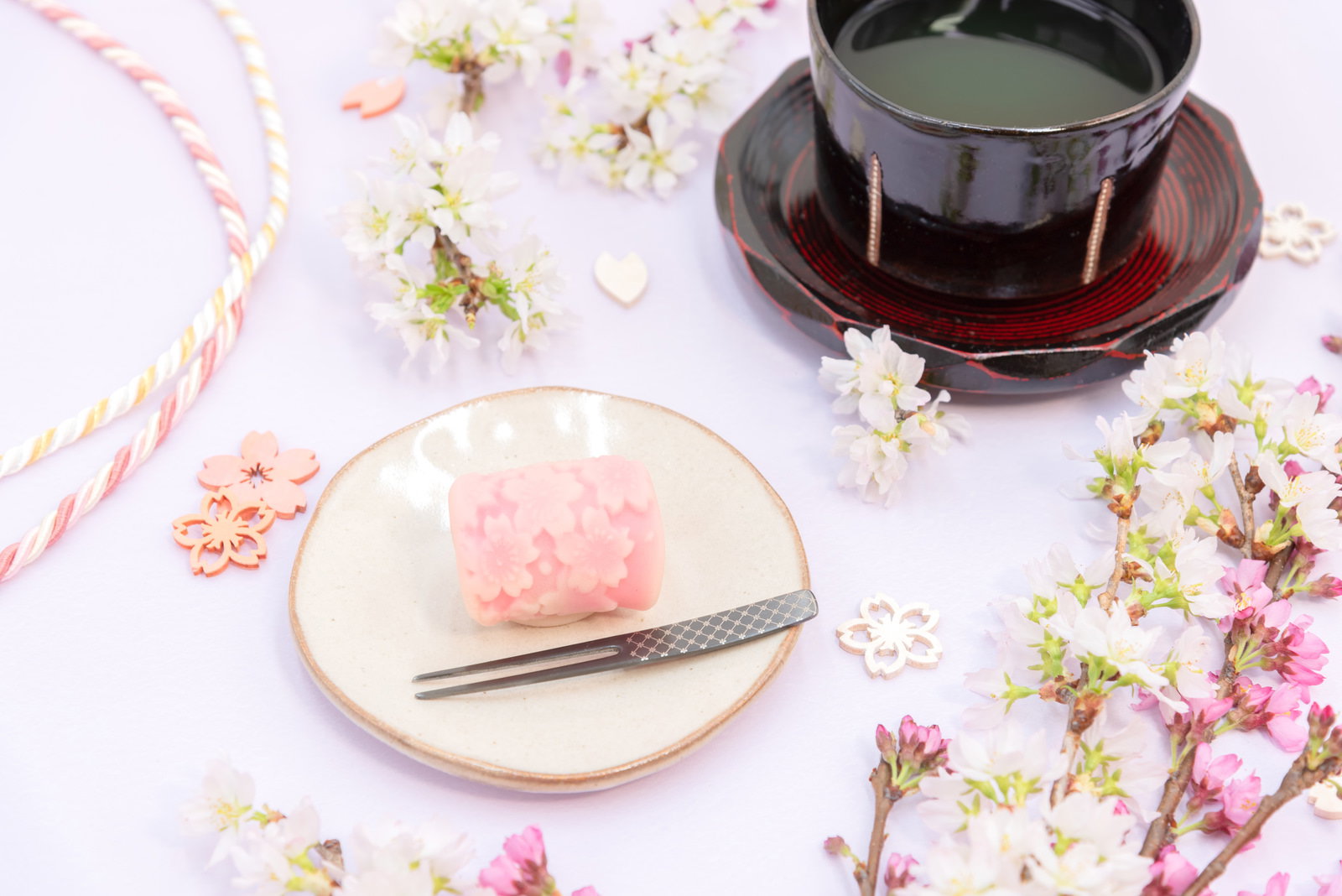 木製のお皿に盛られたピンクの練りきりと抹茶椀、桜の花びらが散らされた和風のテーブルセッティング
