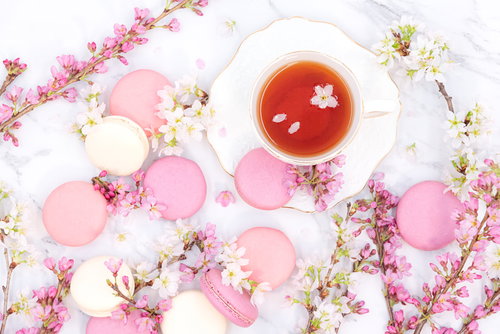 桜の枝に囲まれたピンクと白のマカロンとティーカップ