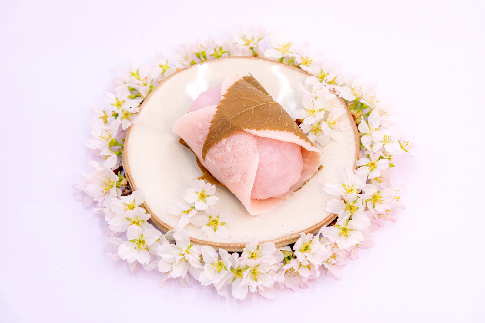 白い皿に盛られた桜餅を桜の花が円形に囲んでいる春らしい和菓子