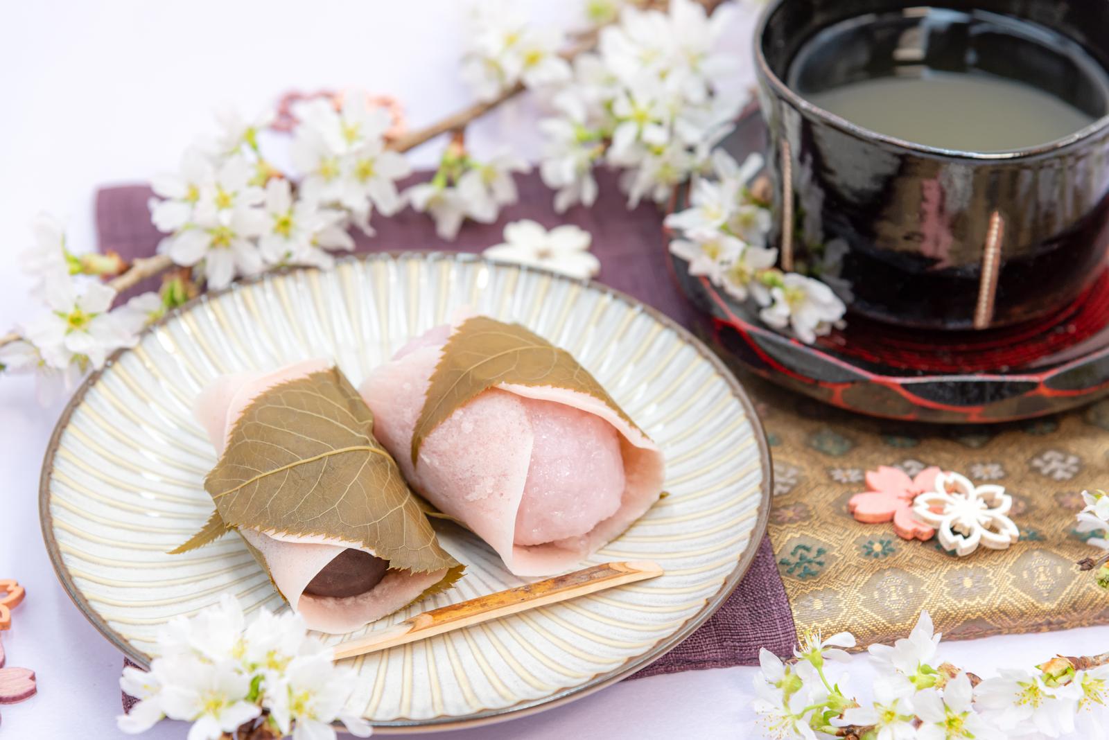 白い皿に盛られた桜もちと抹茶、背景に桜の花