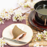 白い小皿に盛られた桜餅と黒い湯呑みの抹茶セットの写真