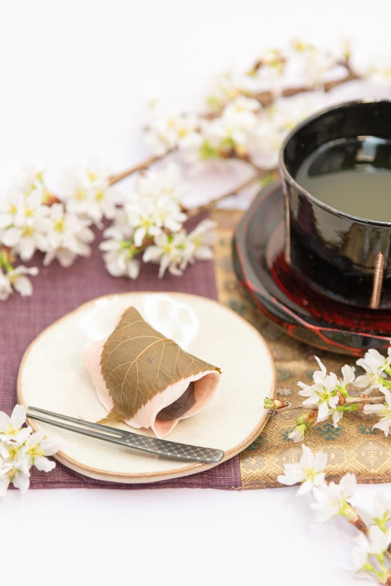 白い皿の上に金色の箸と一緒に盛られた桜餅と黒い湯呑みの抹茶