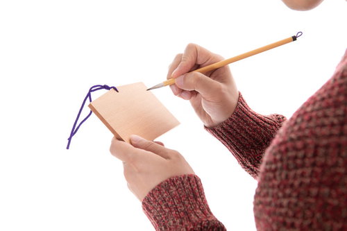 赤いセーターを着た男性が筆で絵馬に願い事を書き込む