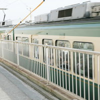 鎌倉高校前駅を通過する江ノ電の緑色車両 踏切を渡るの写真