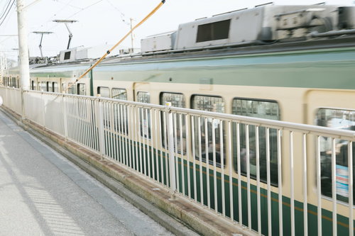 鎌倉高校前駅を通過する江ノ電の緑色車両 踏切を渡る