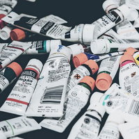 白や赤、黒などのチューブ絵の具が雑多に置かれた画材の写真