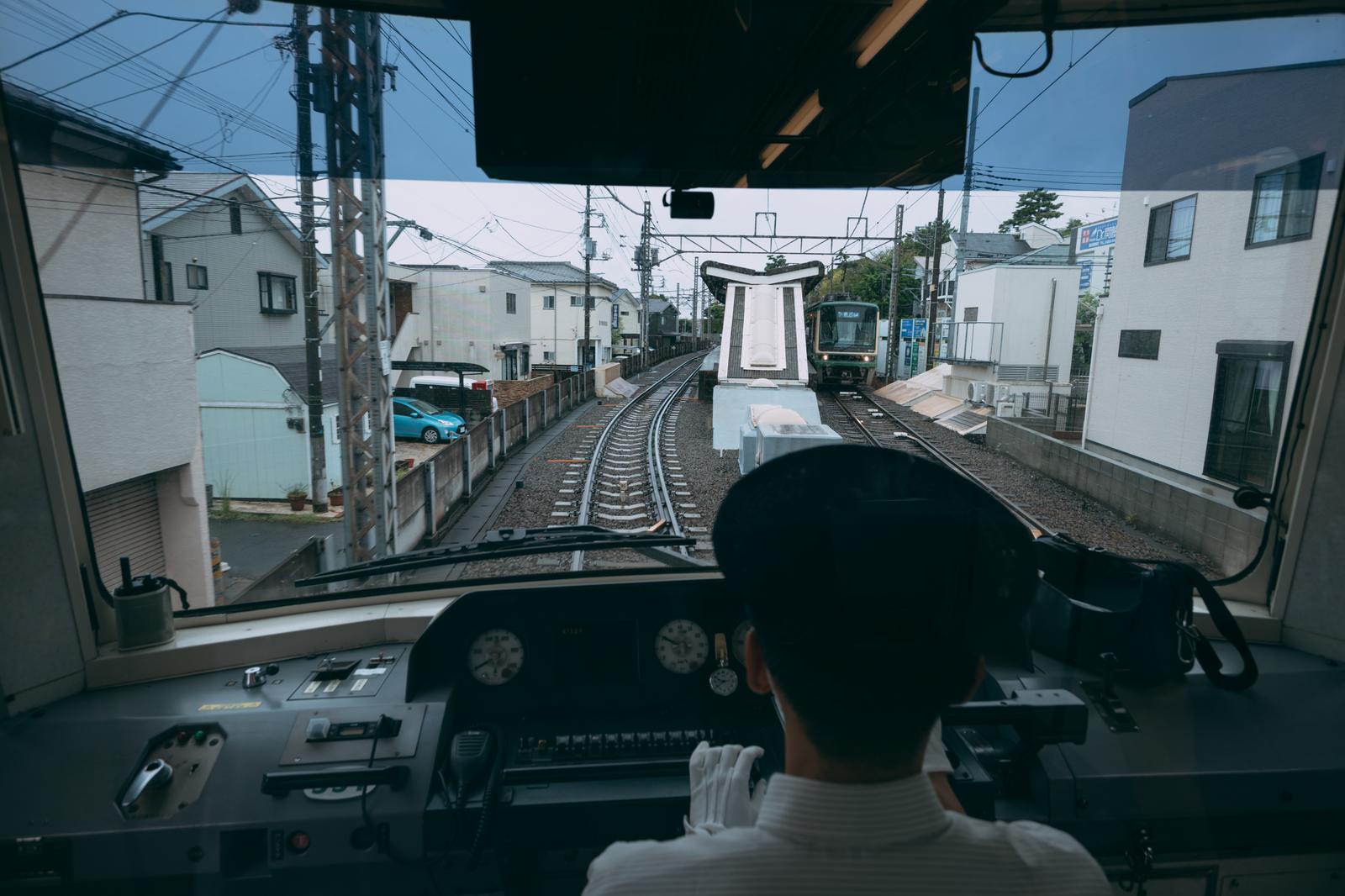 江ノ電の先頭車両から運転士越しに線路と対向電車を望む前面展望