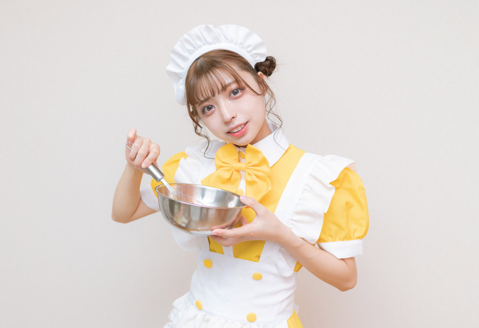 メイド服を着た女性が両手でホイッパーを持って泡立てをしている［モデル：高尾実生］