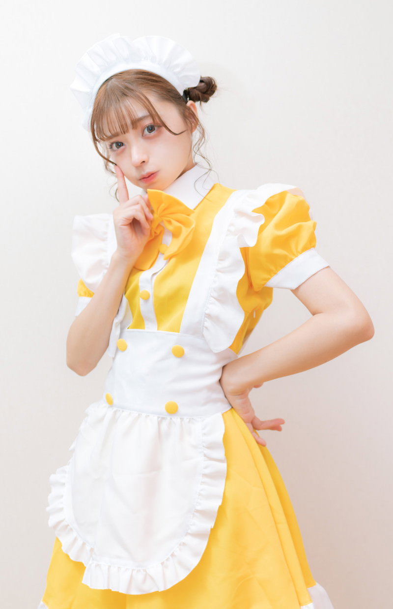 黄色いエプロンドレスを着た女性が人差し指を口元に当てて内緒のポーズをしている［モデル：高尾実生］