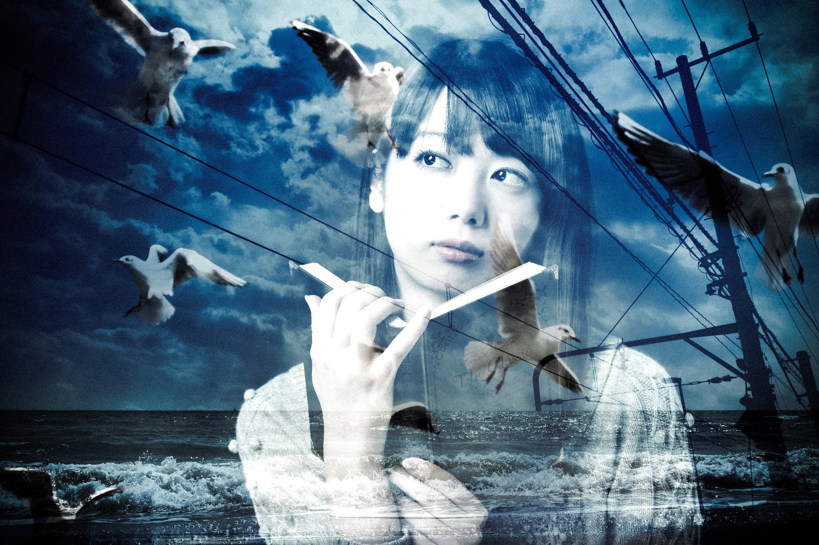 洋書を掲げて上を向く女性の背後に、海、空、カモメ、電線が透けて合成された画像［モデル：モデルリリース］
