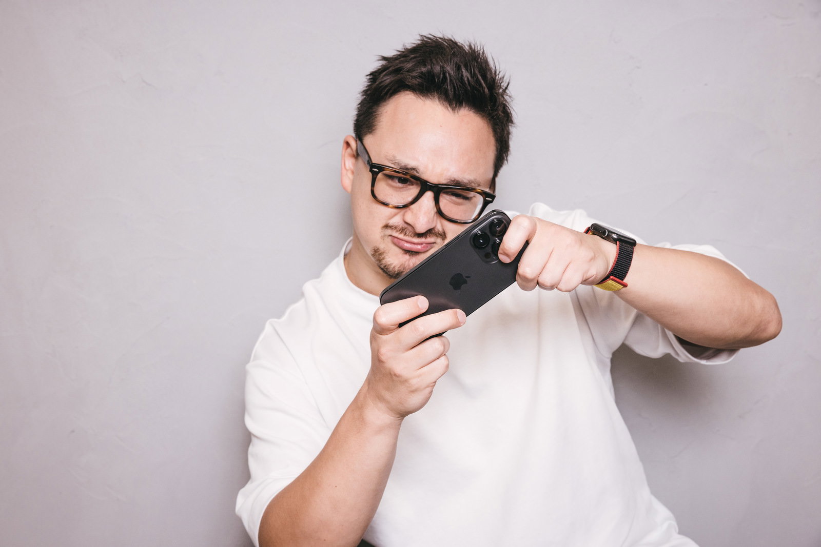 白いTシャツを着た眼鏡の男性がスマートフォンでゲームをプレイしている［モデル：Max_Ezaki］