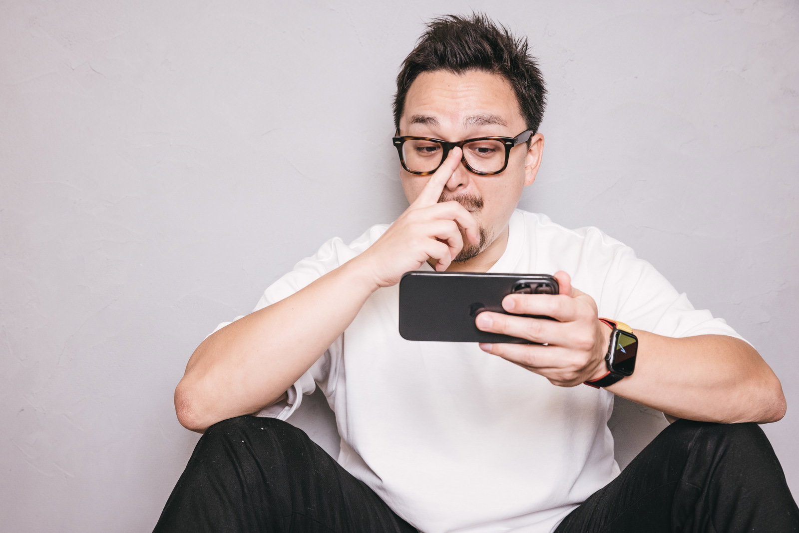 床に座ってスマートフォンを見ながらニヤけた表情をするドイツ人ハーフの男性［モデル：Max_Ezaki］