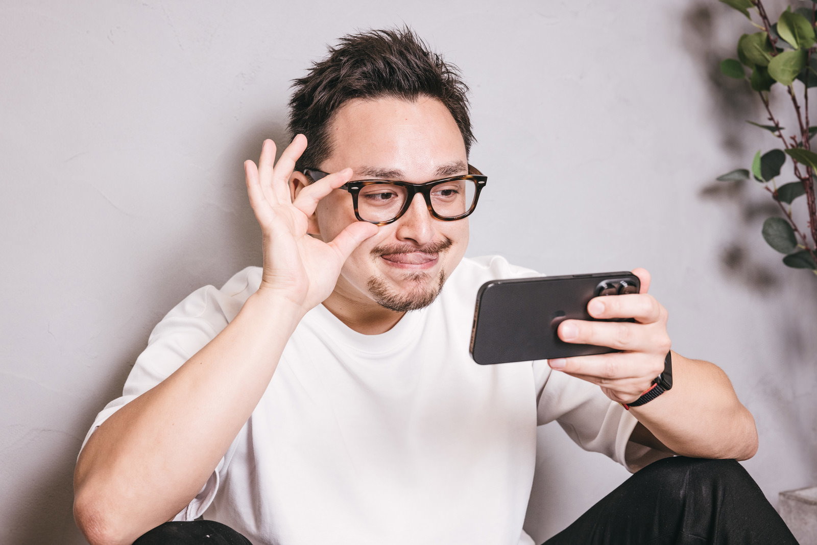 眼鏡をかけた男性がスマホを見ながらニヤけている様子［モデル：Max_Ezaki］