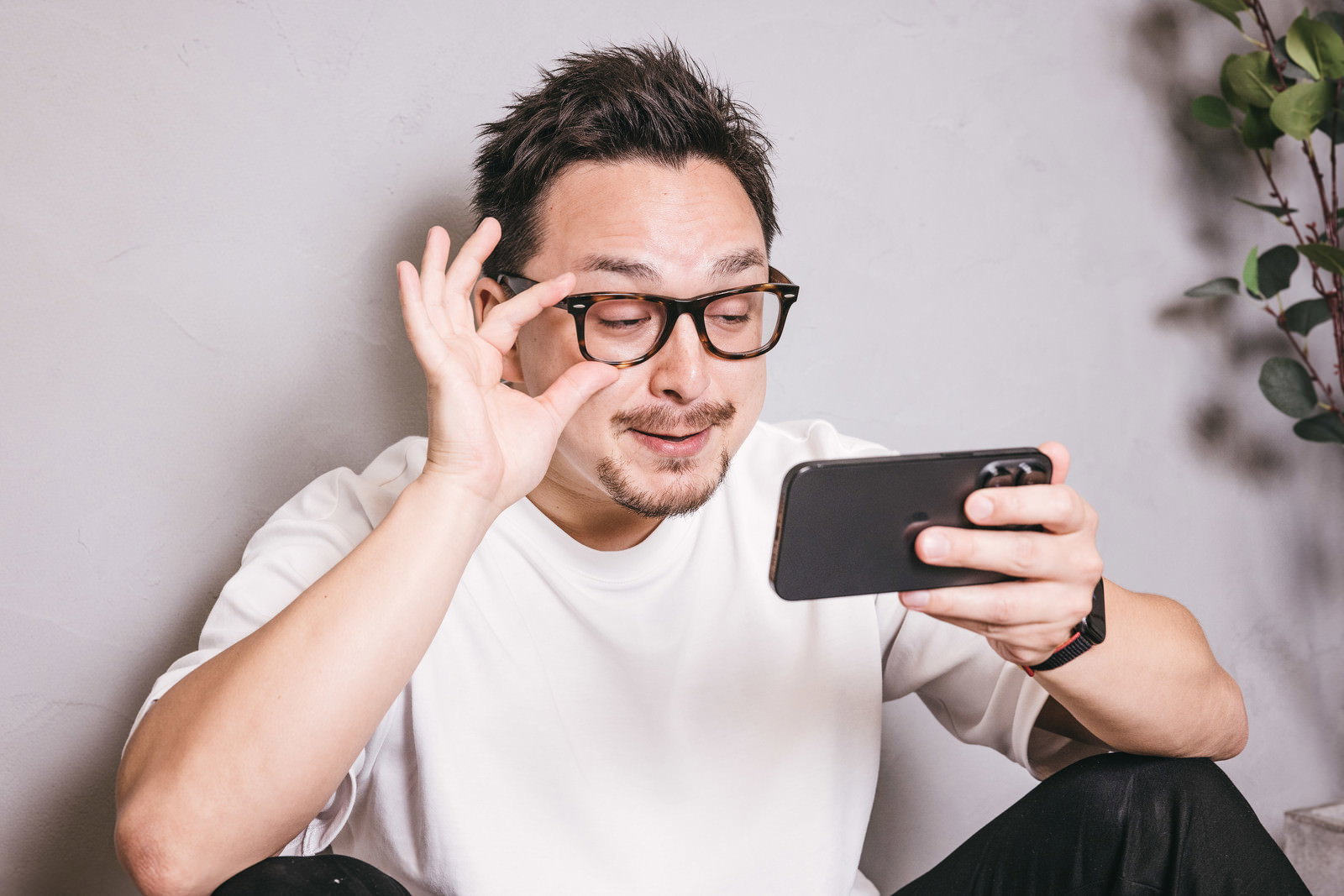スマホを見ながらニヤけた表情を浮かべる眼鏡をかけた男性［モデル：Max_Ezaki］