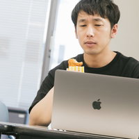 骨なしフライドチキンを食べながらノートパソコンでバグチェックする男性の写真
