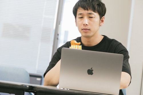 骨なしフライドチキンを食べながらノートパソコンでバグチェックする男性