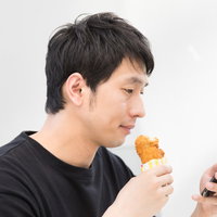 フライドチキンを食べながらスマホでネットサーフィンする男性の写真