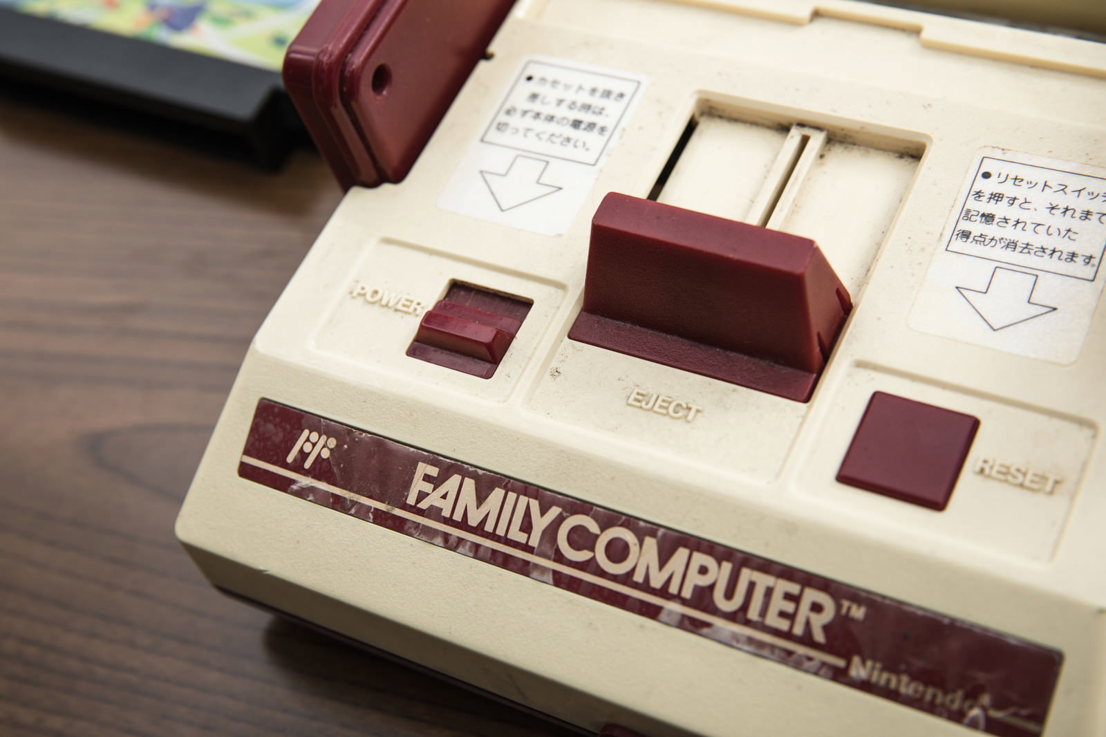 木目のテーブルに置かれた赤白のファミコン本体とコントローラー