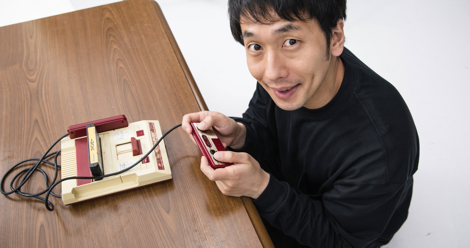 ファミコンのコントローラーを持って笑顔を見せる男性［モデル：大川竜弥］