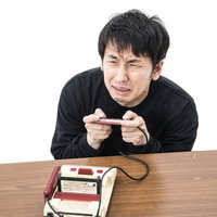 ラスボスに苦戦するゲーマー男性がファミコンコントローラーを握るの写真
