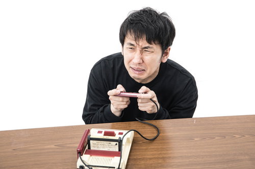 ラスボスに苦戦するゲーマー男性がファミコンコントローラーを握る