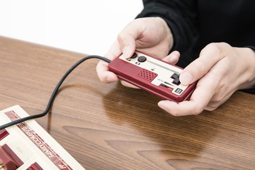 赤いファミコンの2コンで遊ぶ男性の手元のクローズアップ