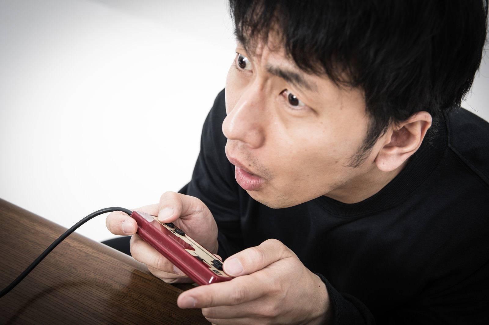 赤いコントローラーを握り困惑した表情を見せる黒い服の男性［モデル：大川竜弥］