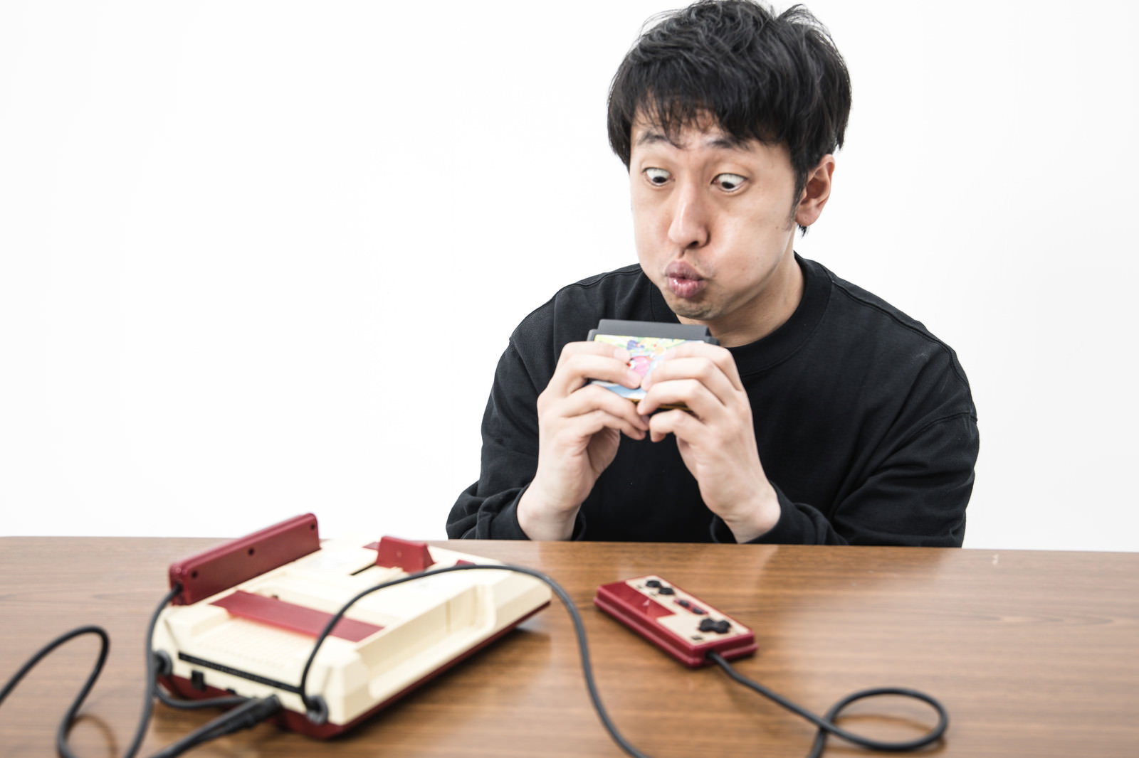 ファミコンカセットに息を吹きかける男性［モデル：大川竜弥］
