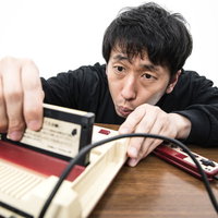 ゲーム機本体にファミコンのカセットを差し込む男性の写真