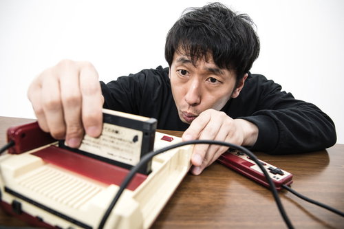 ゲーム機本体にファミコンのカセットを差し込む男性