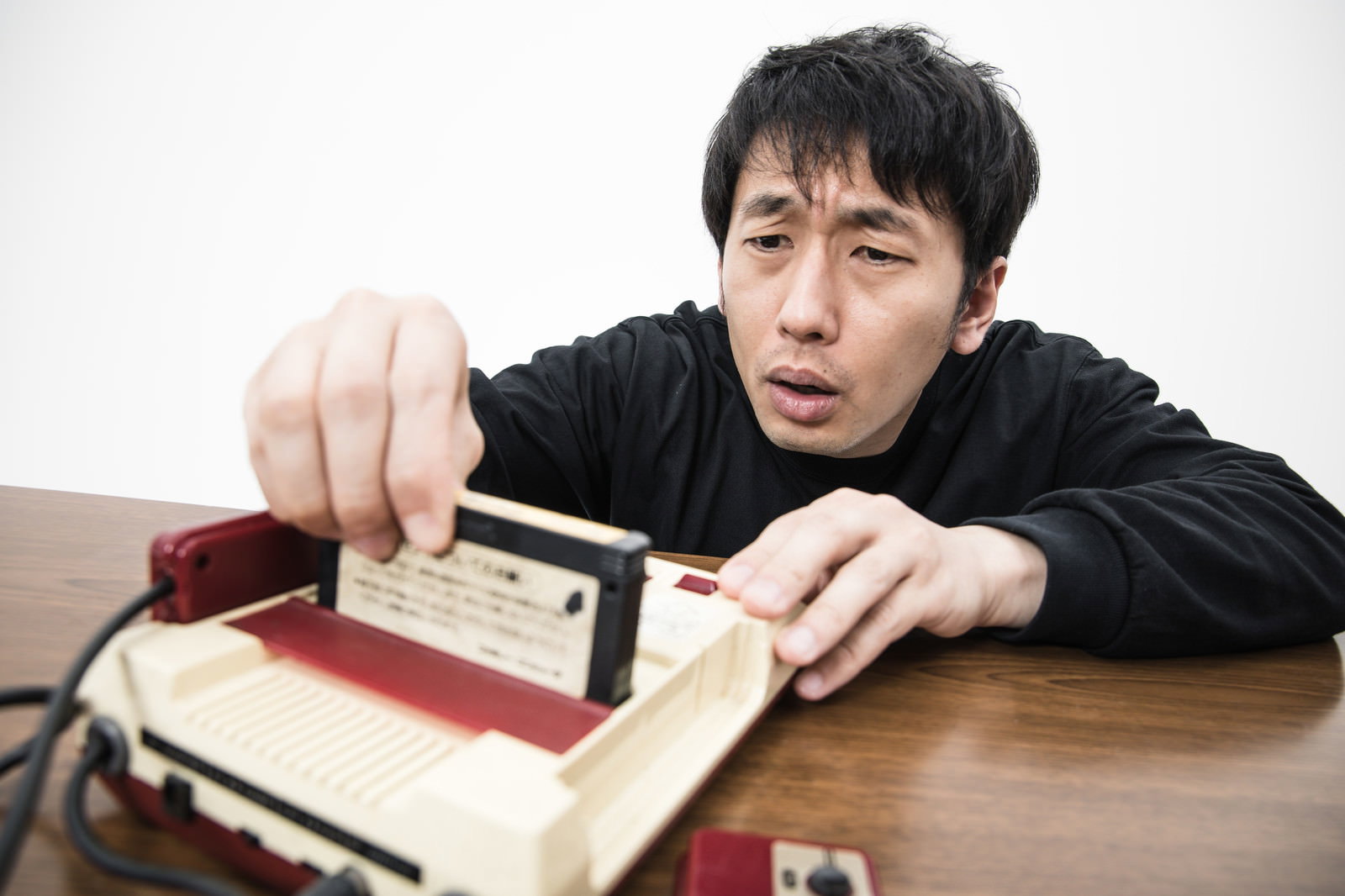 ファミコンの前でゲームカセットを手に持ち困った表情の男性［モデル：大川竜弥］