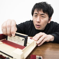 赤いファミコンのカセット角度調整に苦戦するゲーマー男性の写真