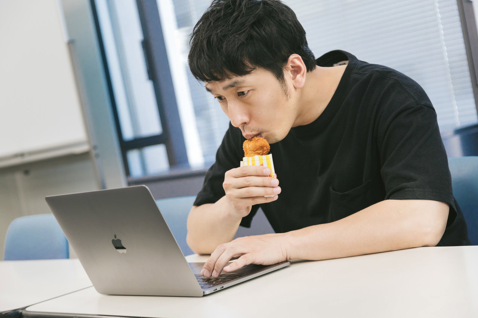 デスクでノートパソコンを使いながらフライドチキンを食べる男性［モデル：大川竜弥］