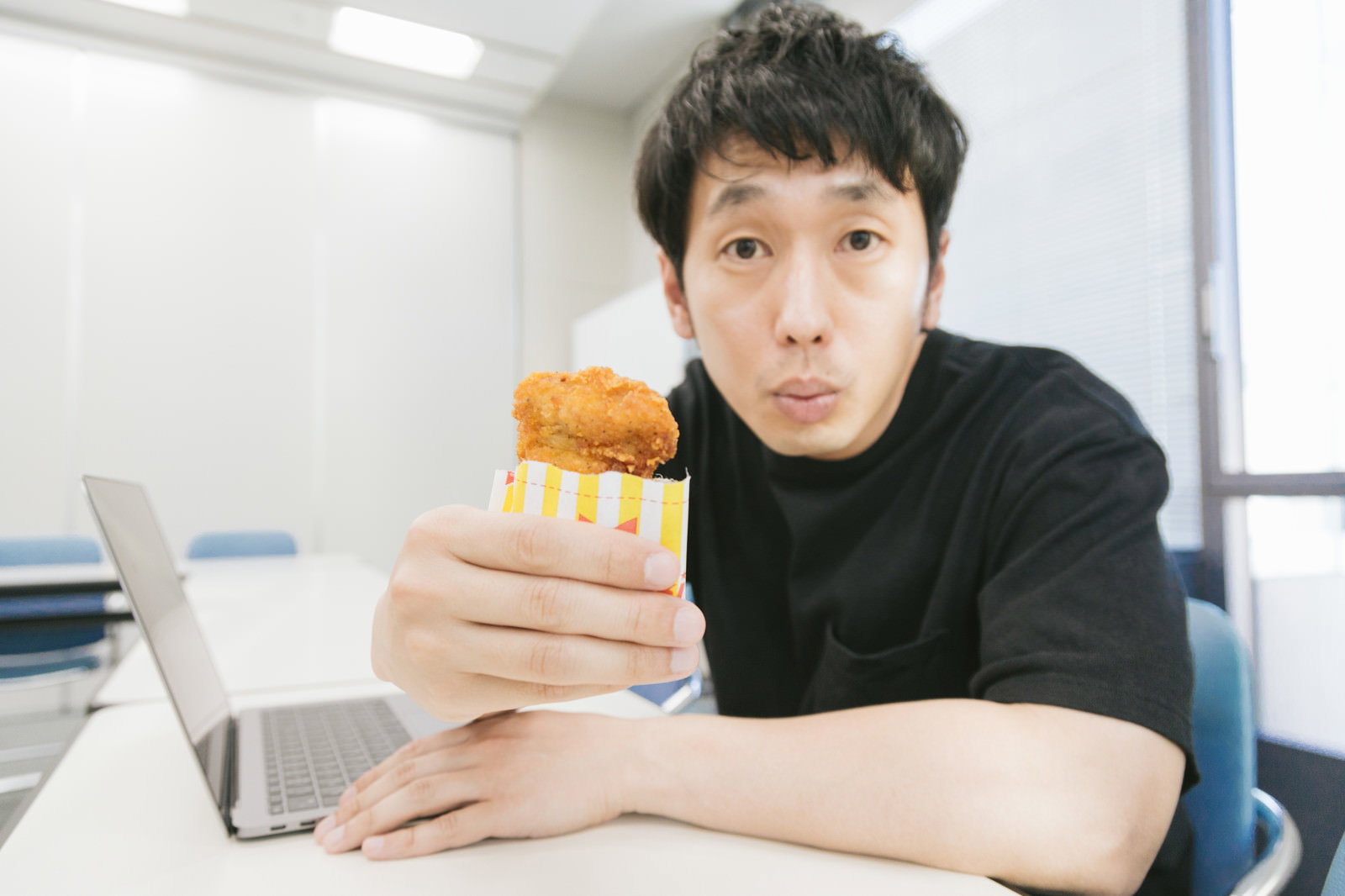 オフィスのデスクで黄白パッケージのフライドチキンを持つ男性［モデル：大川竜弥］