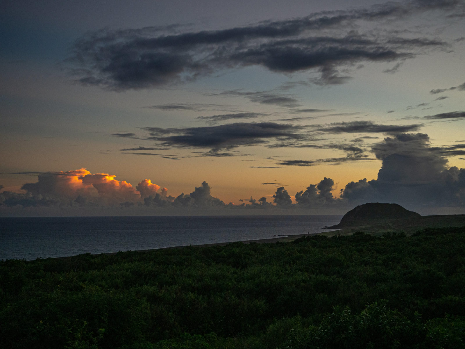 夕焼け空の下、緑の摺鉢山が水平線に浮かぶ日没の風景