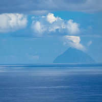 霞むパステル色の海と空の中に三角形の姿を見せる南硫黄島の写真
